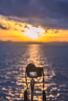 Colorful image with a DSLR camera on a tripod capturing, in live view mode, a beautiful sunset over the water.
