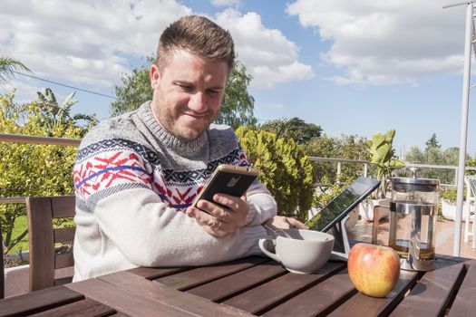 Happy man having breakfast with technology in the garden