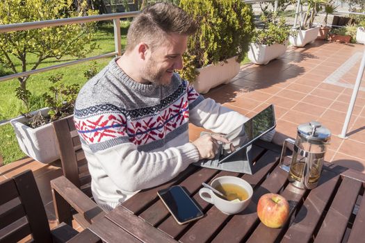 Happy man having breakfast with technology in the garden