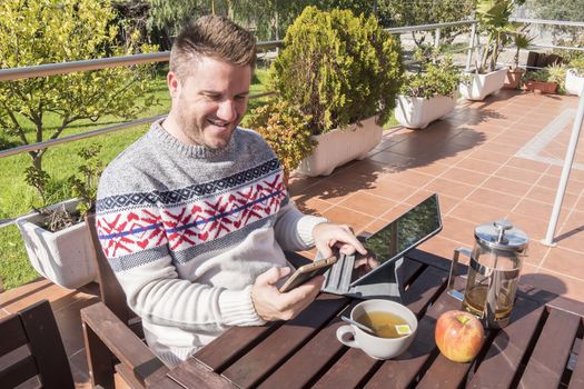 Happy man having breakfast with technology in the garden