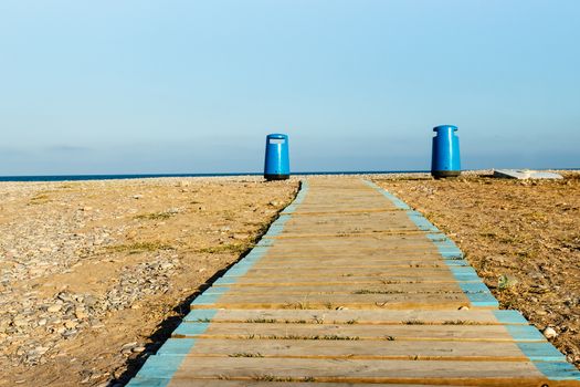 Wooden walkway on the beach with two litter bins in the background. Horizontal image