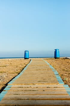 Wooden walkway on the beach with two litter bins in the background. Vertical image.