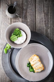 Fried cod fillets and spinach on a wooden surface