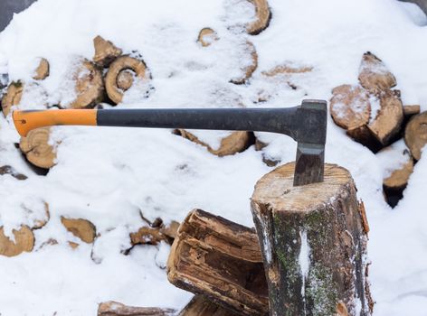 The ax stuck in a tree stump on a background of chopped firewood stored in the winter
