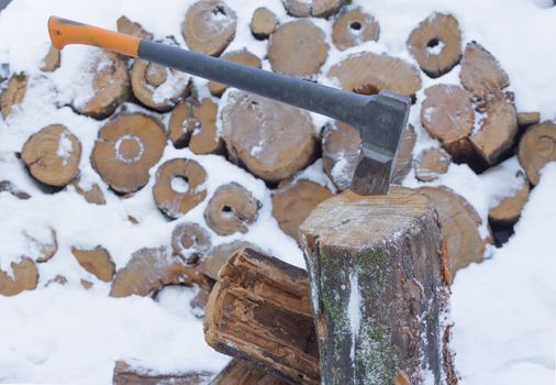 The ax stuck in a tree stump on a background of chopped firewood stored in the winter