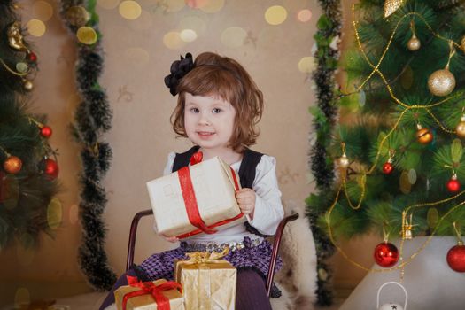 Cute girl sitting on sledge and holding gift-box under Christmas tree