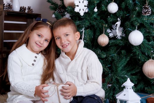 Sister and brother sittting together under Christmas tree