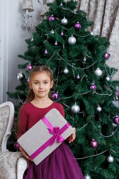 Pretty girl holding magenta gift-box under christmas tree