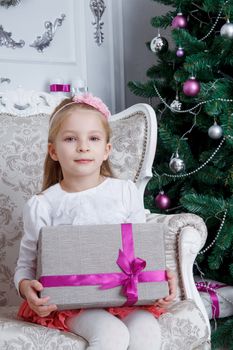 Pretty girl holding gift-box sitting under Christmas tree