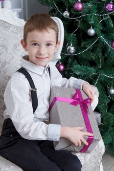 Happy smiling boy with present under Christmas tree