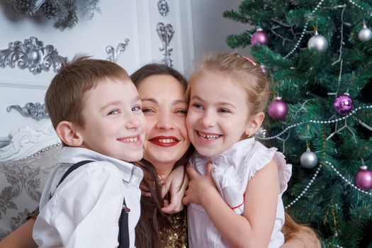 Two kids cheek to cheek with their mother under Christmas tree