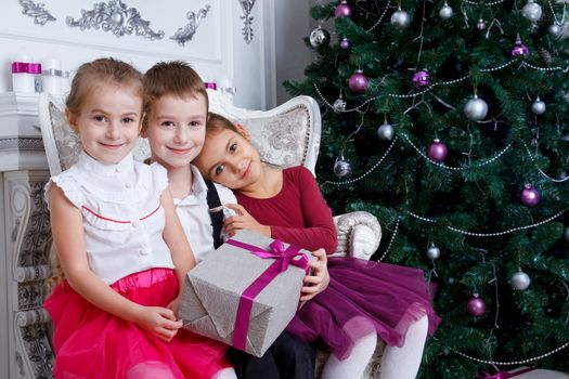 Three kids sitting under Christmas magenta tree with gift-box