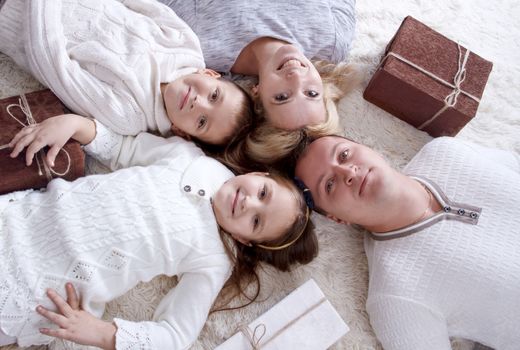 Happy family with two kids and giftboxes lying on the floor and looking at camera