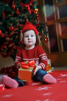 Pretty baby girl with red gift near Christmas tree