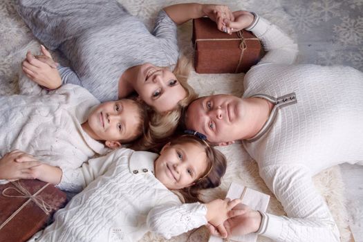 Happy family with two children and giftboxes lying on the floor and looking at camera