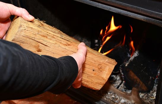 Man hands putting the log to the burning fireplace. Man stoking the wood into fireplace.