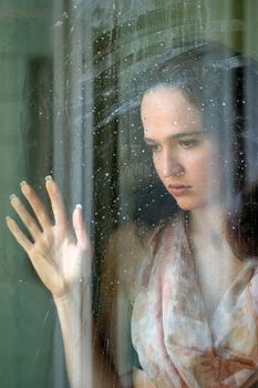 Woman with sad smile behind a wet window