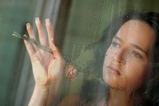 Woman with sad smile behind a wet window