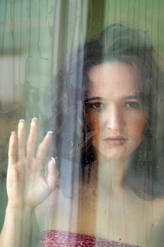 Woman with sad smile behind a wet window