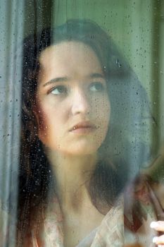 Woman with sad smile behind a wet window