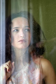 Woman with sad smile behind a wet window