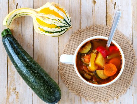 Minestrone soup on the wooden background, with pumpkin and zucchini lying next to the soup. Soup prepared with summer-autumn vegetables such as: zucchini, pumpkin, carrot, paprika, runner beans etc.