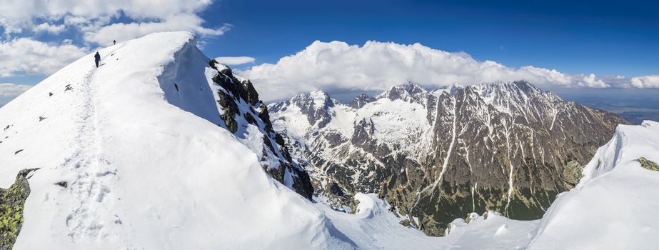 Mountain panorama. Two climbers going thru snow towards the summit. Footpath. Sky is clear. Good weather. High Tatras Slovakia