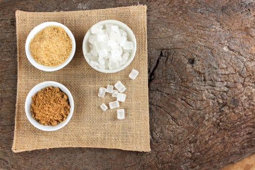 Brown cane sugar and granulated sugar and rock sugar in a cup on old wood.