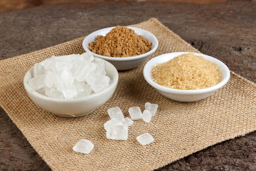 Brown cane sugar and granulated sugar and rock sugar in a cup on old wood. 