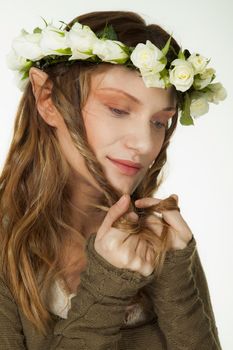 A portrait of a beautiful woman with wreath of roses and elfs ears playing with her long hair.