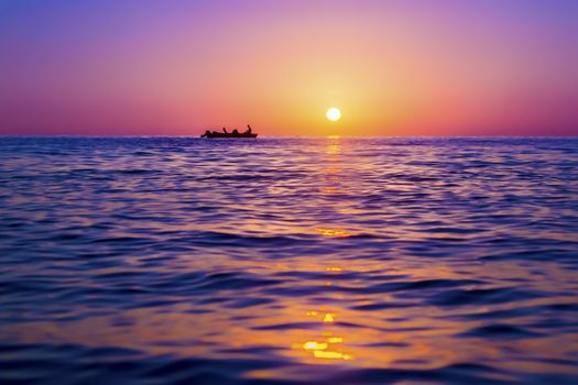 Evening seascape. Silhouette of man on the boat against the setting sun. The sun reflected off the waves. Purple, pink and yellow colors
