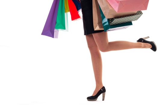 Lower close-up of running woman wearing short skirt and shoes with high hills holding multicolored shopping paper bags and packages, isolated on white background