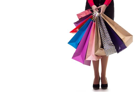 Lower close-up of standing woman wearing short skirt and shoes with high hills holding multicolored shopping paper bags and packages, isolated on white background