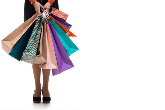 Lower close-up of standing woman wearing short skirt and shoes with high hills holding multicolored shopping paper bags and packages, isolated on white background