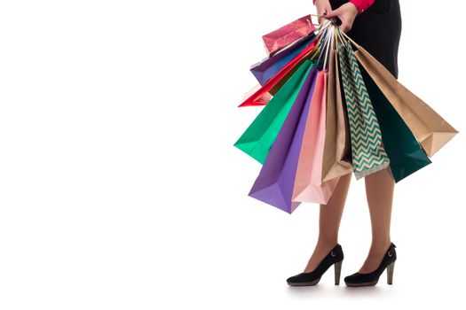 Lower close-up of standing woman wearing short skirt and shoes with high hills holding multicolored shopping paper bags and packages, isolated on white background