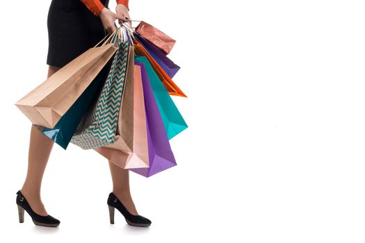Lower close-up of walking woman wearing short skirt and shoes with high hills holding multicolored shopping paper bags and packages, isolated on white background
