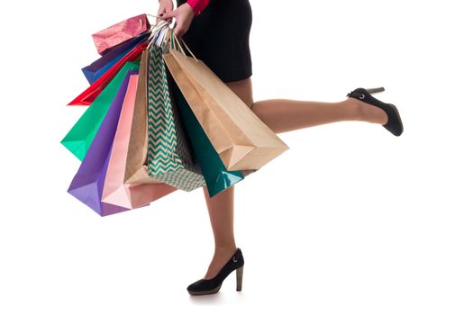 Lower close-up of running woman wearing short skirt and shoes with high hills holding multicolored shopping paper bags and packages, isolated on white background