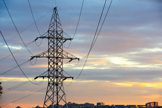 Electricity pylons and power lines silhouettes at a cloudy sunset over urban skyline