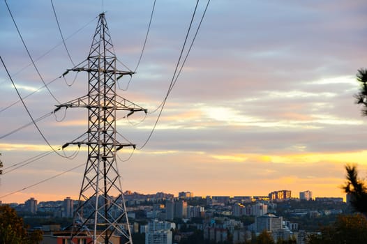 Electricity pylons and power lines silhouettes at a cloudy sunset over urban skyline