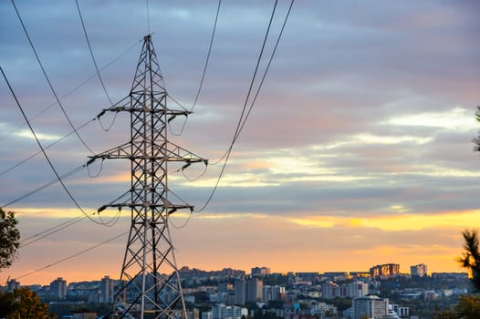 Electricity pylons and power lines silhouettes at a cloudy sunset over urban skyline