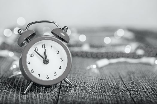 Christmas composition - red alarm clock on a textured wooden board with lights and beads bokeh