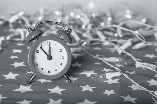Christmas composition - red alarm clock with lights bokeh on a red fabric background with stars ornament