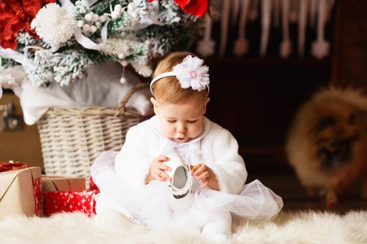 Portrait of a beautiful little girl in a white dress and wrap hair with a flower in the interior with Christmas decorations