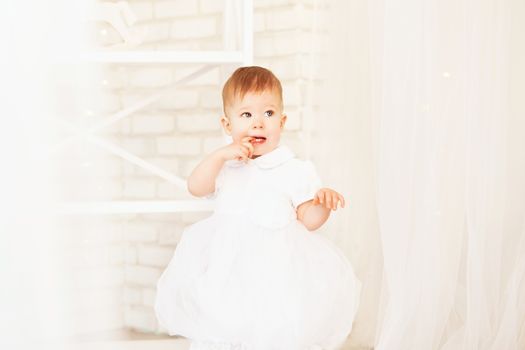 Portrait of a beautiful baby girl in a white dress in the interior with Christmas decorations