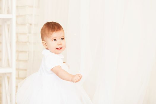 Portrait of a beautiful baby girl in a white dress in the interior with Christmas decorations