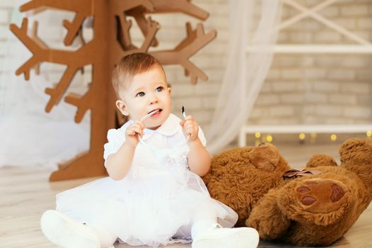 Portrait of a beautiful baby girl with a soft brown teddy bear in the interior with Christmas decorations.