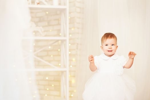 Portrait of a beautiful baby girl in a white dress in the interior with Christmas decorations