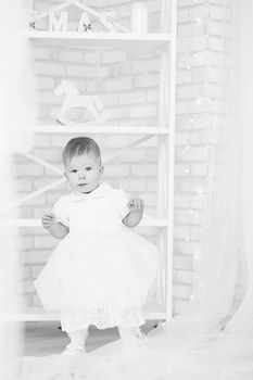 Portrait of a beautiful baby girl in a white dress in the interior with Christmas decorations. Black and white photography