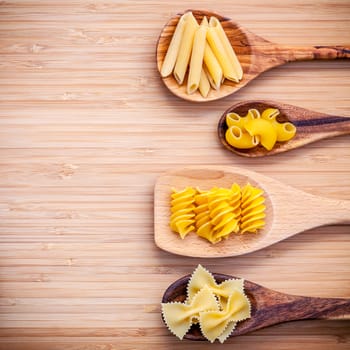 Italian foods concept and menu design . Various kind of Pasta Elbow Macaroni ,Farfalle ,Rigatoni ,Gnocco Sardo in wooden spoons setup on bamboo cutting board with flat lay.