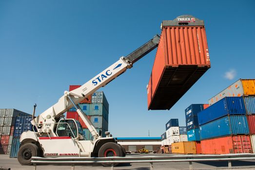 Forklift truck lifting cargo container in shipping yard or dock yard against sunrise sky, France